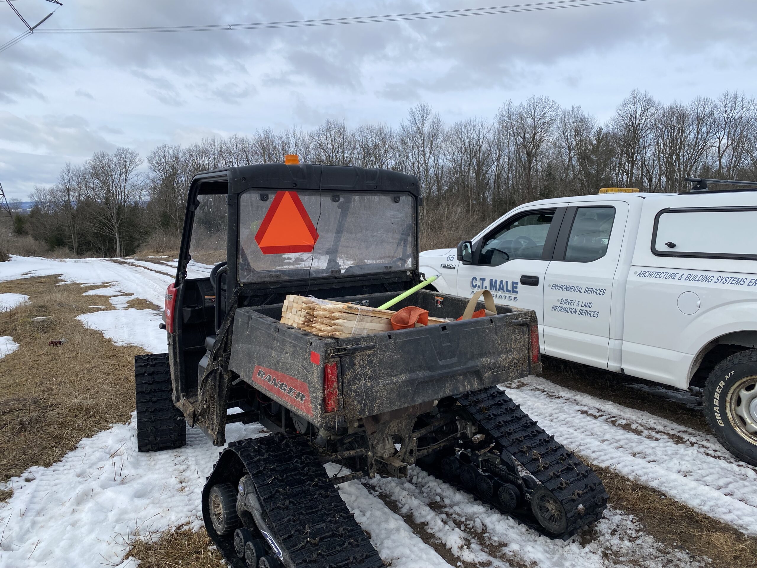 All-terrain vehicle with track wheels next to a C.T. Male truck